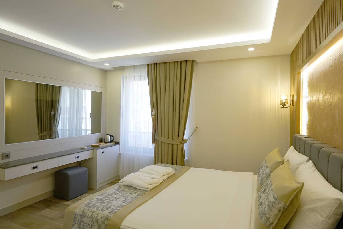Une chambre d’hôtel comprenant un lit, une table de chevet, un miroir, une fenêtre avec des rideaux et un luminaire fixé au mur.