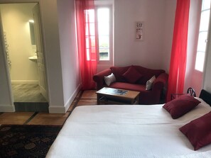 Un dormitorio con una cama grande, un sofá rojo, una mesita y una ventana con cortinas rojas.