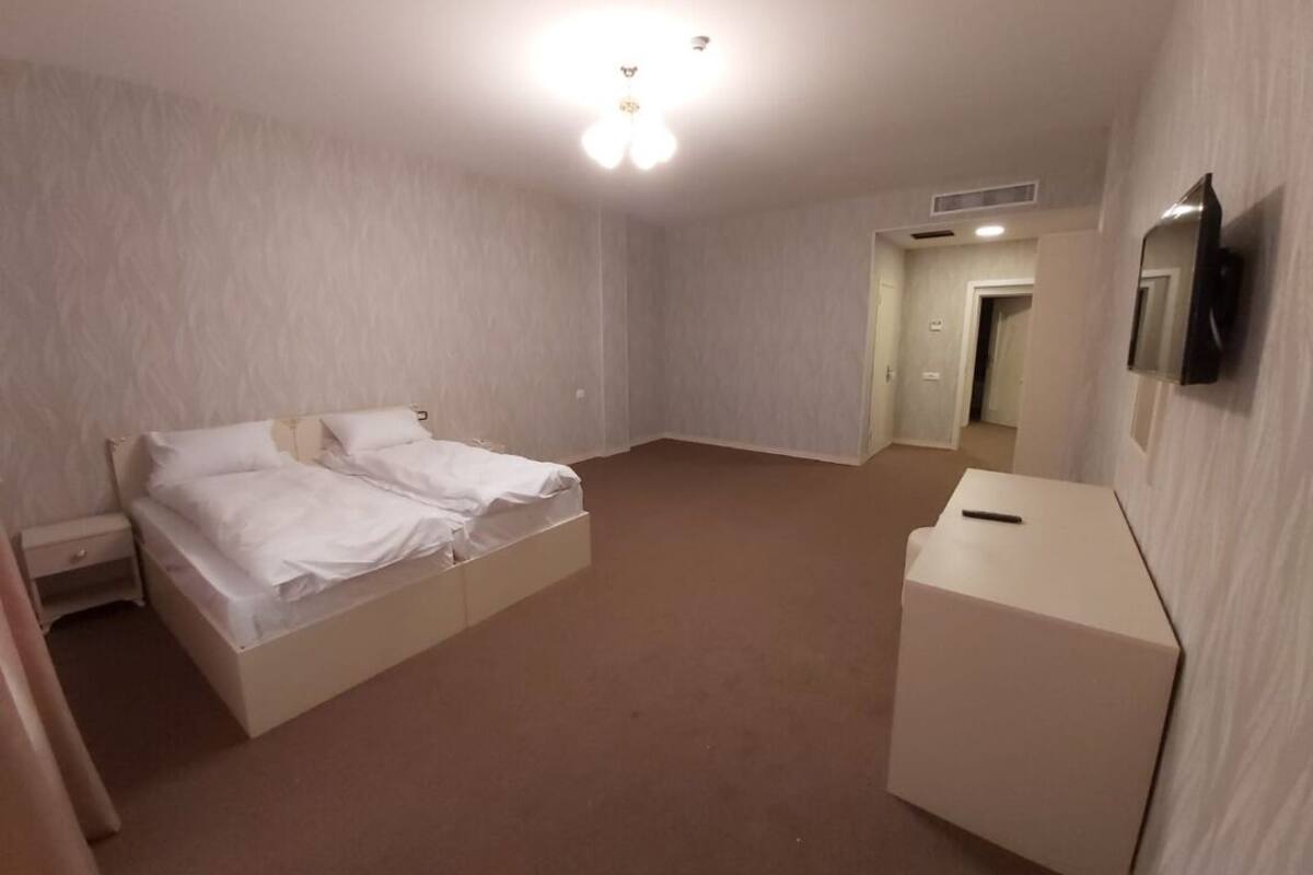 A hotel room with a double bed, a small bedside table, a desk, and a flat-screen TV mounted on the wall.