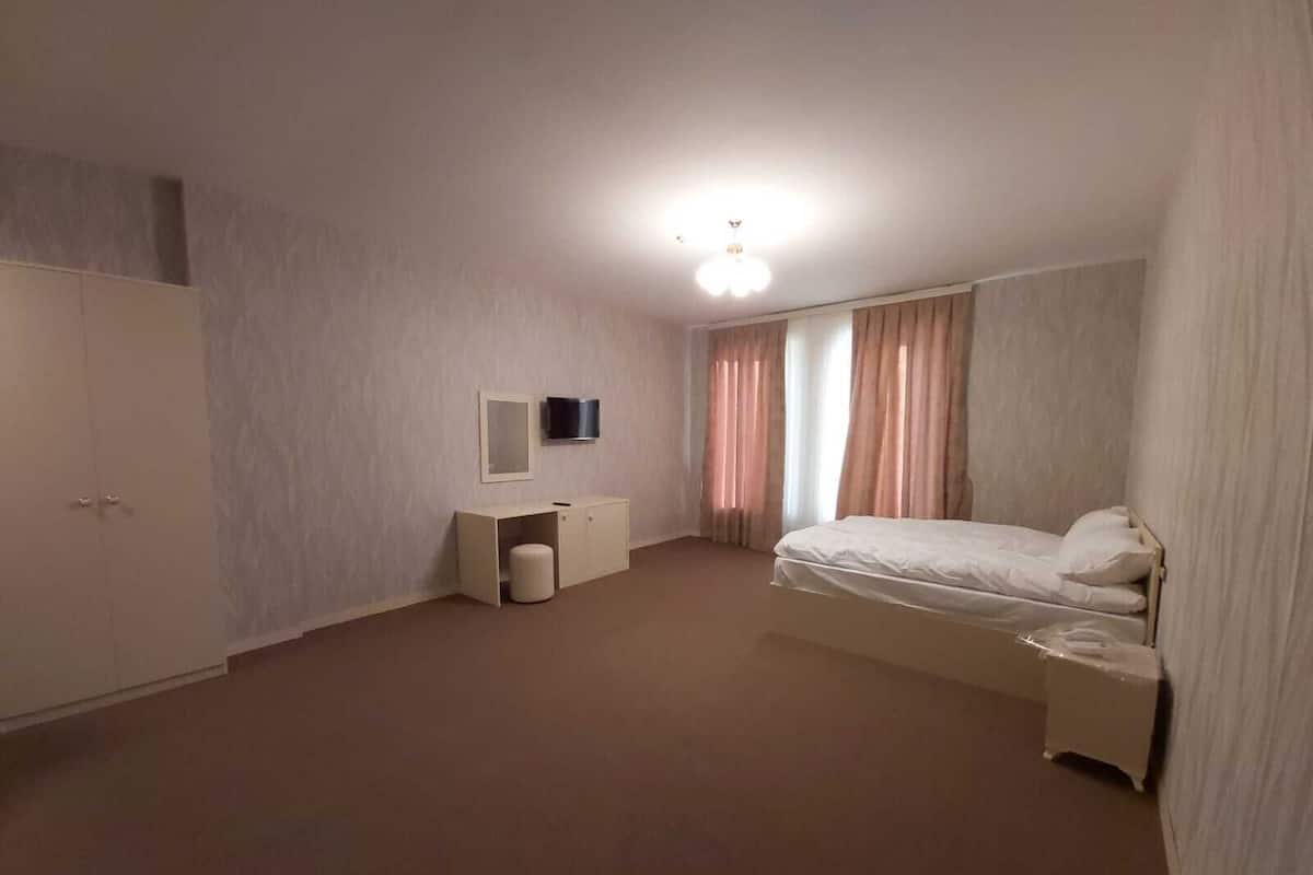 A bedroom with a bed, a desk, a wardrobe, and a ceiling light.