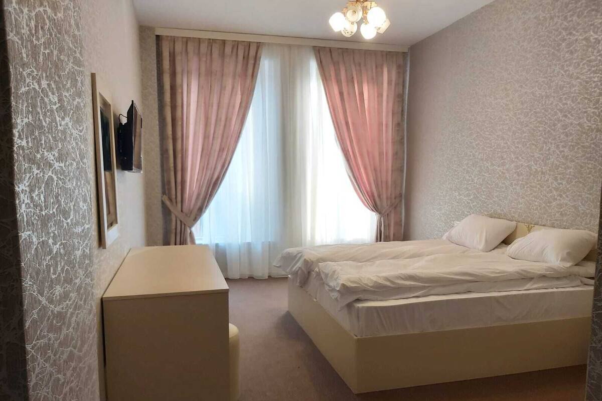 A bedroom with a bed, a desk, and a window with curtains.