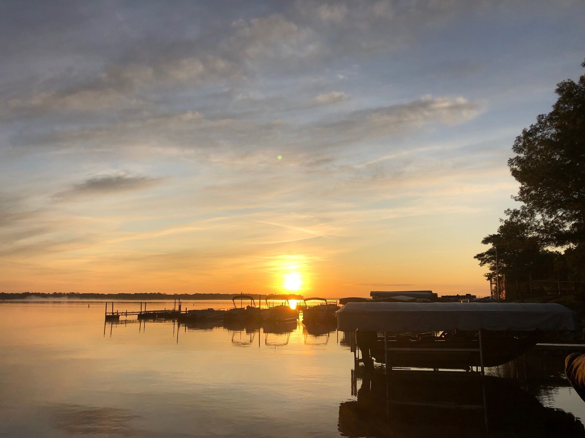 En stilla sjö vid solnedgången, med båtar förtöjda och en brygga som sträcker sig ut i vattnet.