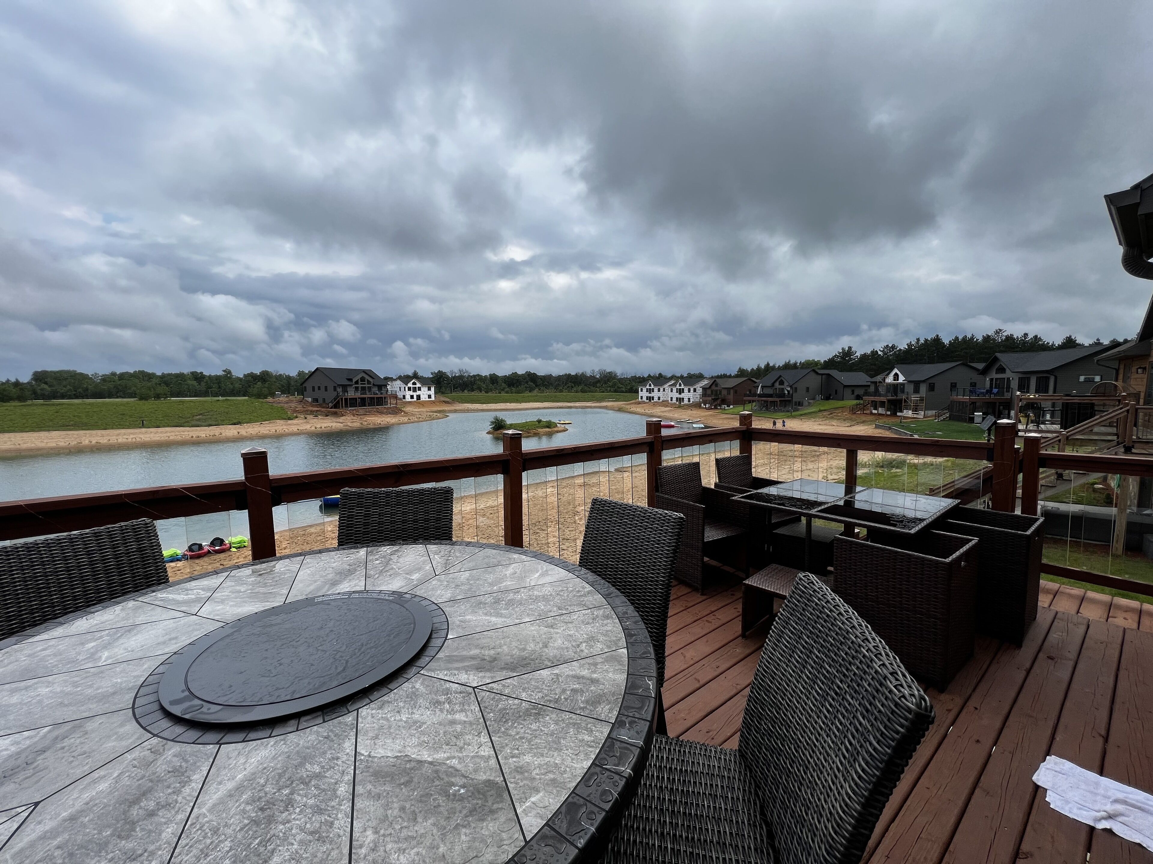 Eine Terrasse mit einem Steintisch und Korbstühlen, die auf einen See blickt, mit Häusern im Hintergrund.