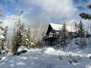 Une cabane dotée d’un balcon, entourée d’arbres couverts de neige et surplombant un ciel dégagé.