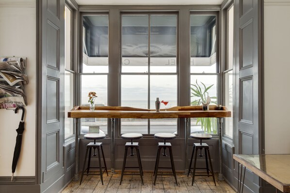Ein Zimmer mit einem langen Holztisch, drei Hocker und einem großen Fenster mit Aussicht.