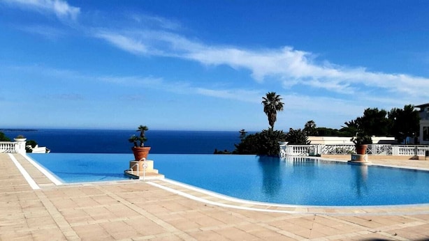 Una piscina con vista sull'oceano, circondata da un recinto bianco e piante in vaso.