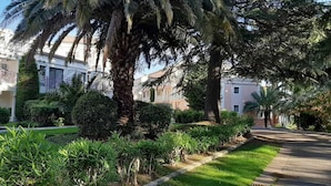 Una zona residenziale con un giardino curato, un vialetto lastricato e una fila di edifici bianchi con balconi.