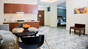 A modern kitchen with wooden cabinets, a dining table with chairs, a fruit bowl, and a small refrigerator. - Dabi Hotel & Apartments (Addis Ababa)