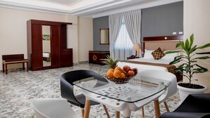 A hotel room with a bed, a desk, a chair, a table with fruit, and a potted plant. - Dabi Hotel & Apartments (Addis Ababa)