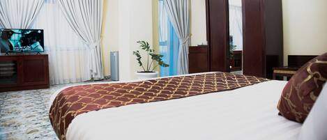 Habitación de hotel con cama, cortinas, televisor, planta en maceta y armario.