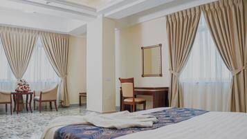 Ein Hotelzimmer mit einem Bett, einem Schreibtisch, einem Stuhl und einem kleinen Tisch mit Blumenvase.