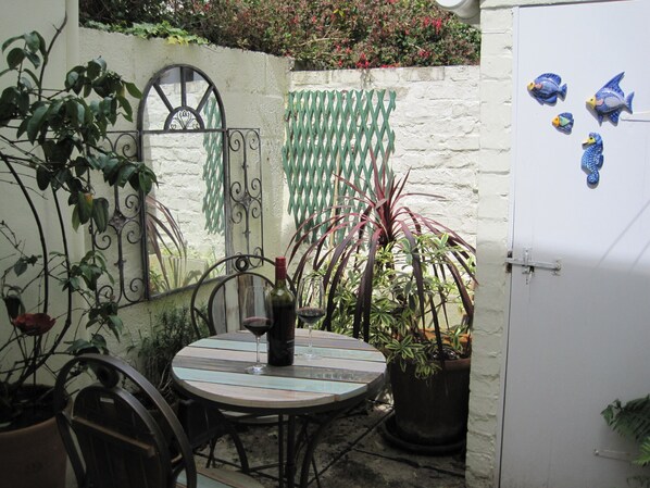 A patio with a round table, chairs, a wine bottle, and potted plants. - Quayside Fishermans Cottage (Appledore)