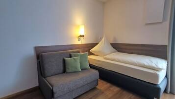 Une petite chambre d’hôtel avec un canapé, un lit et une lampe fixée au mur.