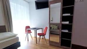 Moderni huone, jossa on sänky, työpöytä, kaksi tuolia, televisio ja vaatekaappi.