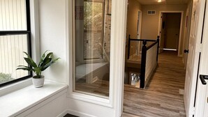 Ein Flur mit Holzboden, einem Blumentopf auf einer Fensterbank und einer Glastür, die in einen anderen Raum führt.