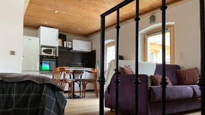Kodikas olohuone, jossa on violetti sohva, ruokapöytä tuoleineen ja taustalla keittiö.