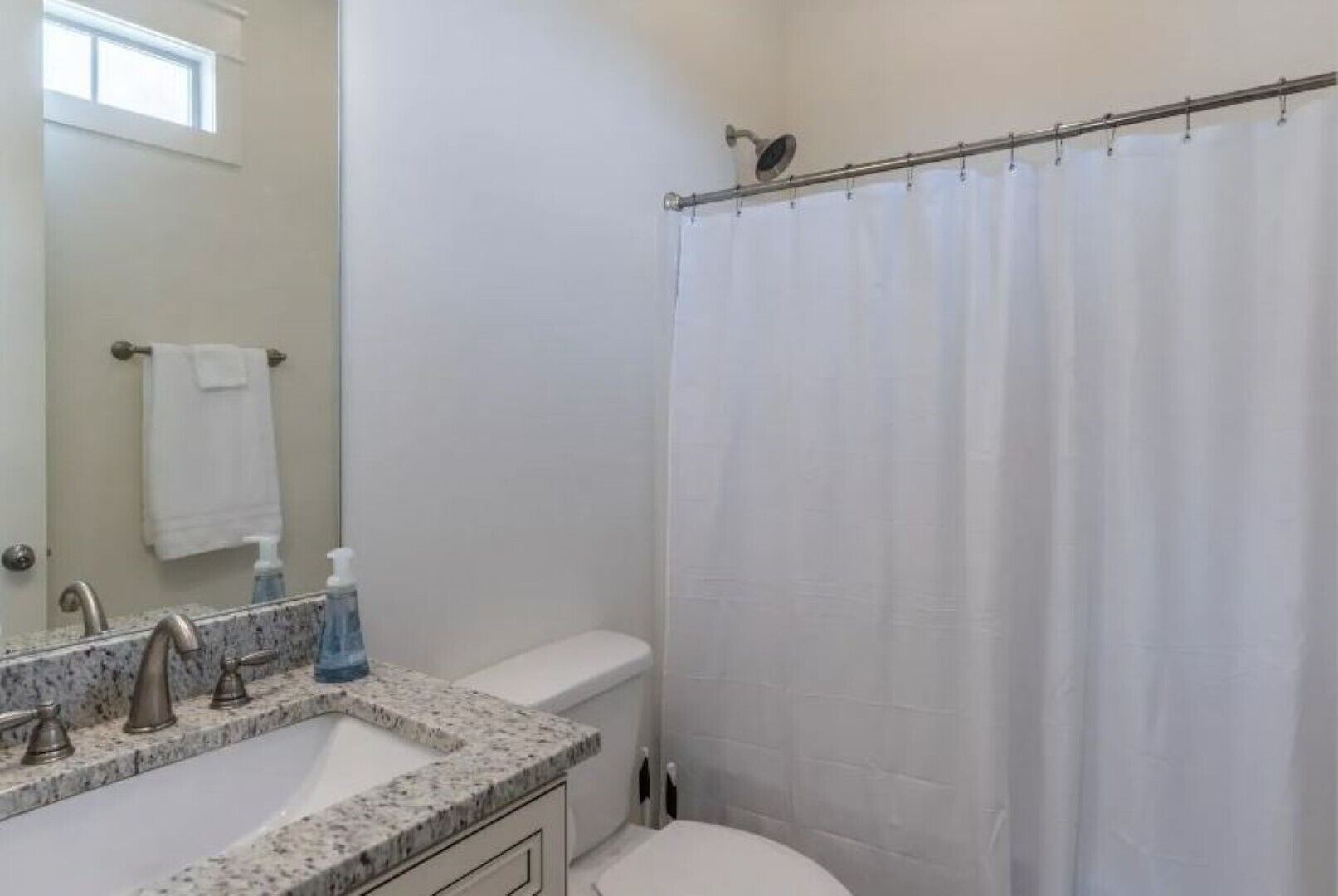 Une salle de bain avec des toilettes blanches, un lavabo doté d’un plan de travail en granit, un miroir et un rideau de douche.