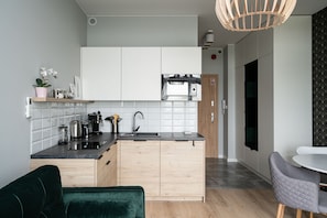 A modern kitchen with white cabinets, a black countertop, and a built-in microwave. There is a green chair and a small table with a white tablecloth. - RentPlanet - Apartamenty Zarembowicza (Wroclaw)