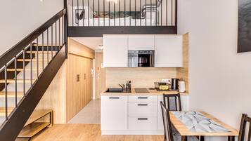 A modern kitchen with a built-in oven, white cabinets, and a wooden dining table.