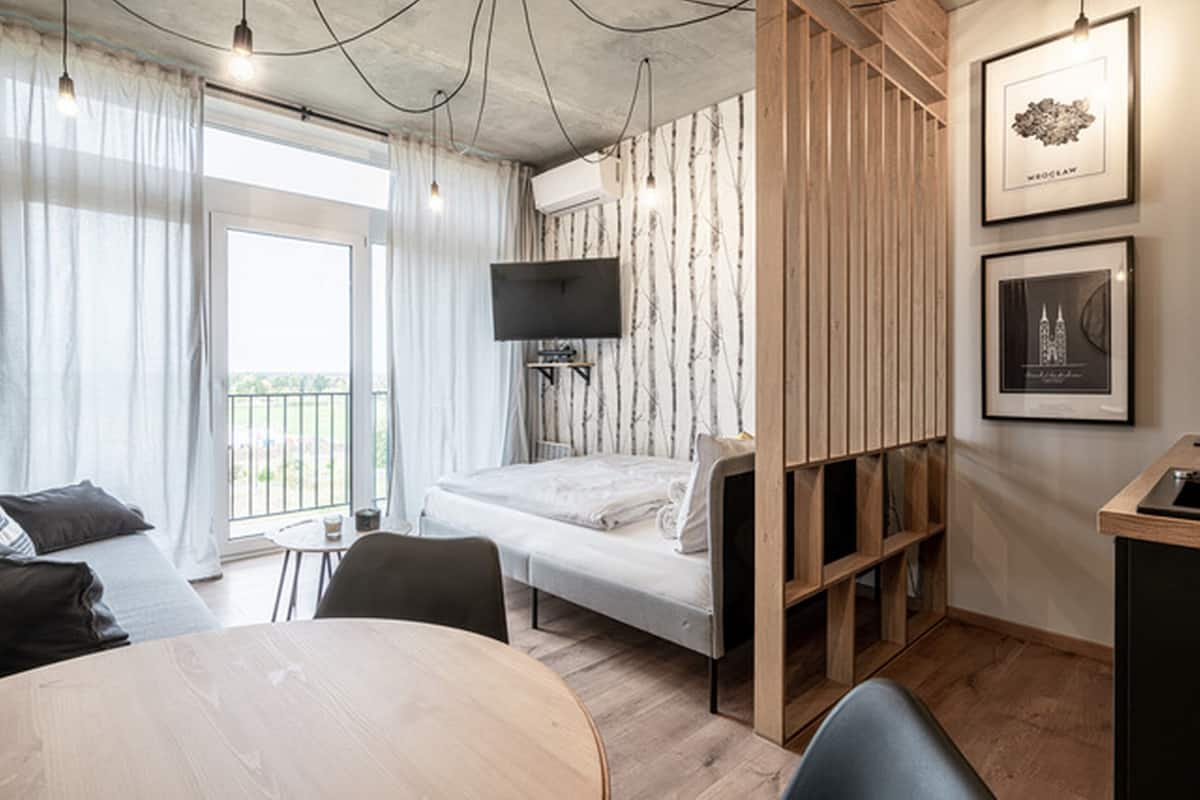 A modern bedroom with a bed, a TV, a desk, and a dining table.