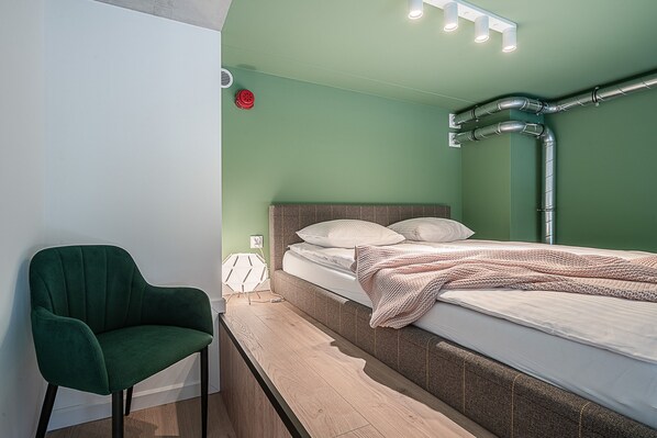 Une pièce avec un lit, une chaise verte et un banc en bois.