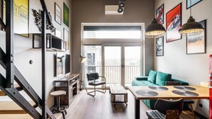 A modern living space with a staircase, a dining area with a table and chairs, a green sofa, and a balcony with a view. - RentPlanet - Apartamenty Zarembowicza (Wroclaw)