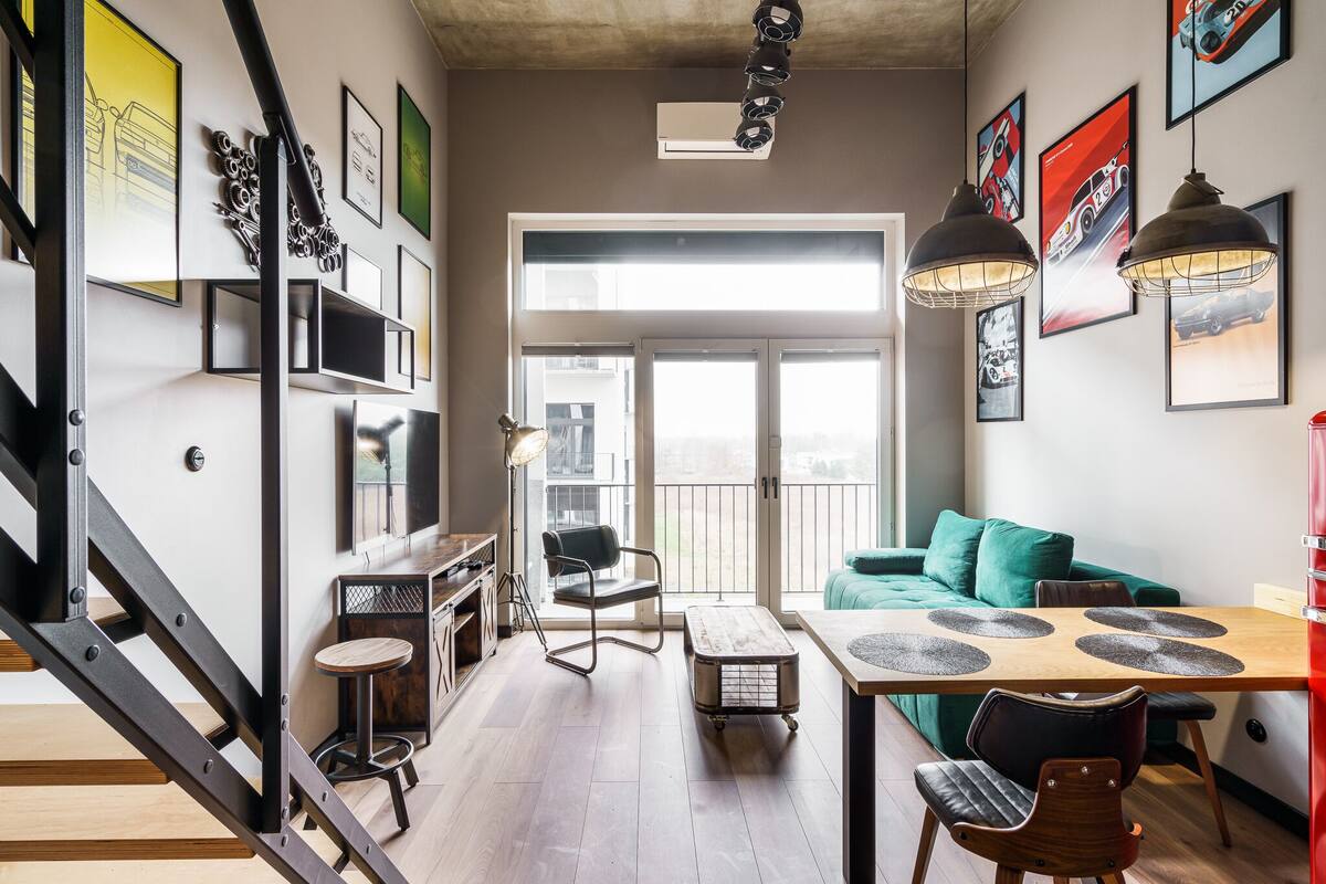 A modern living space with a staircase, a dining area with a table and chairs, a green sofa, and a balcony with a view.