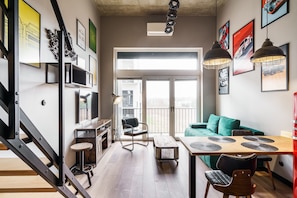 A modern living space with a staircase, a dining area with a table and chairs, a green sofa, and a balcony with a view. - RentPlanet - Apartamenty Zarembowicza (Wroclaw)