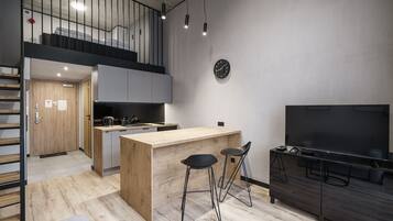 Une cuisine moderne avec un îlot central en bois, deux tabourets de bar, un grand téléviseur à écran plat et un escalier menant à un niveau supérieur.