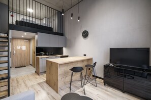 A modern kitchen with a wooden island, two bar stools, a large flat-screen TV, and a staircase leading to an upper level. - RentPlanet - Apartamenty Zarembowicza (Wroclaw)