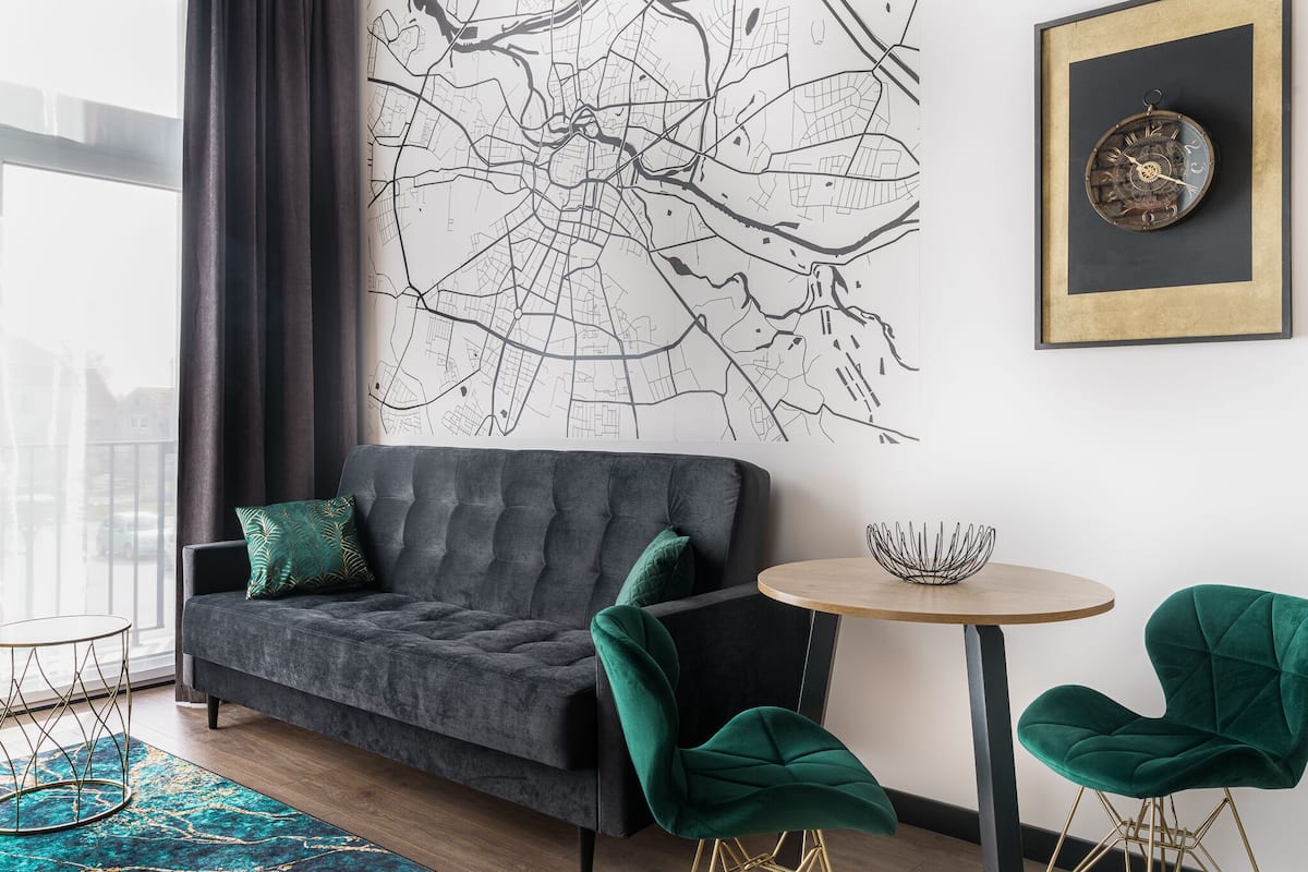 A modern living room with a grey sofa, green chairs, a round table, and a cityscape wall art.