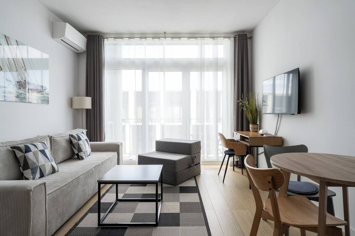A modern living room with a sofa, ottoman, coffee table, and dining area with chairs and a table.