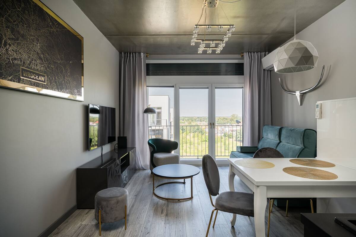 A modern living room with a dining area, large windows, and a view of greenery.