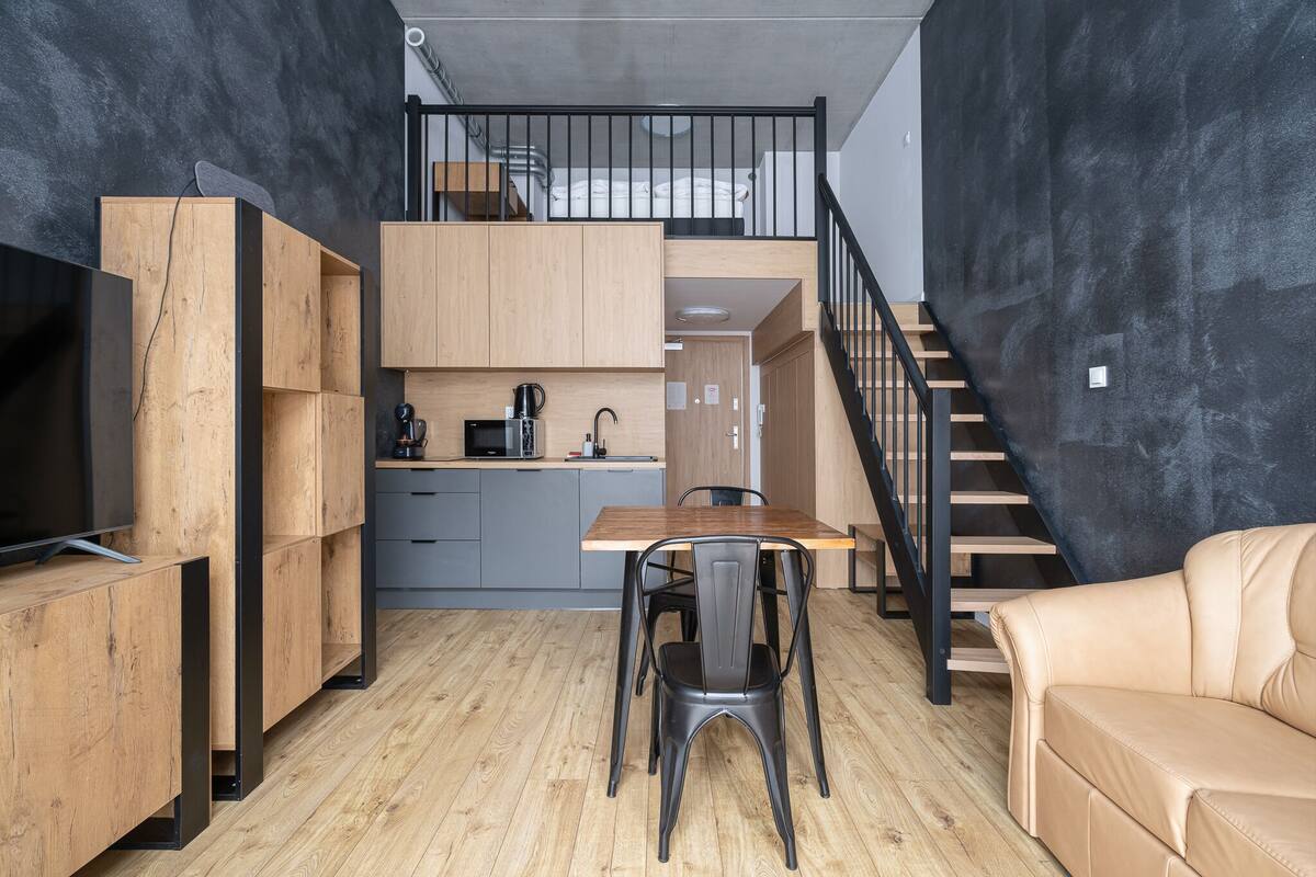 A compact living space with a kitchenette, a dining area, a sofa, and a staircase.