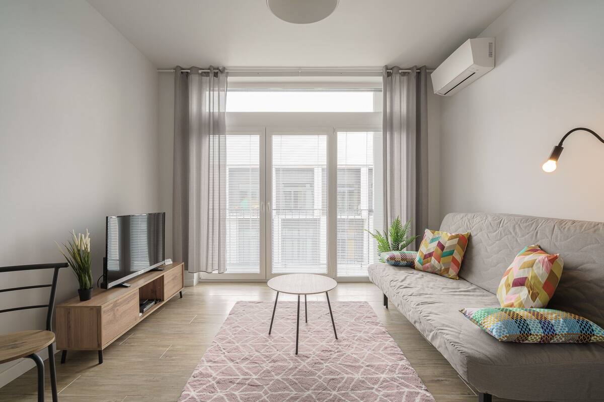 A modern living room with a sofa, a TV on a wooden stand, a small round table, and a patterned rug.