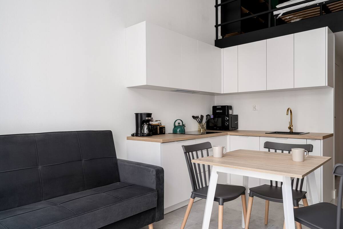 A modern kitchen with white cabinets, a black countertop, and a wooden dining table with four chairs.