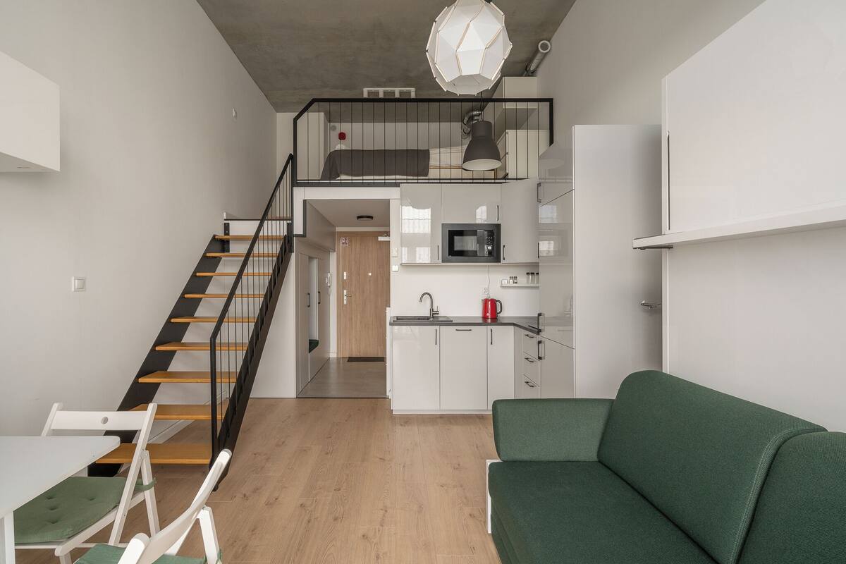 A modern apartment with a staircase, a kitchen, a dining area, and a green sofa.
