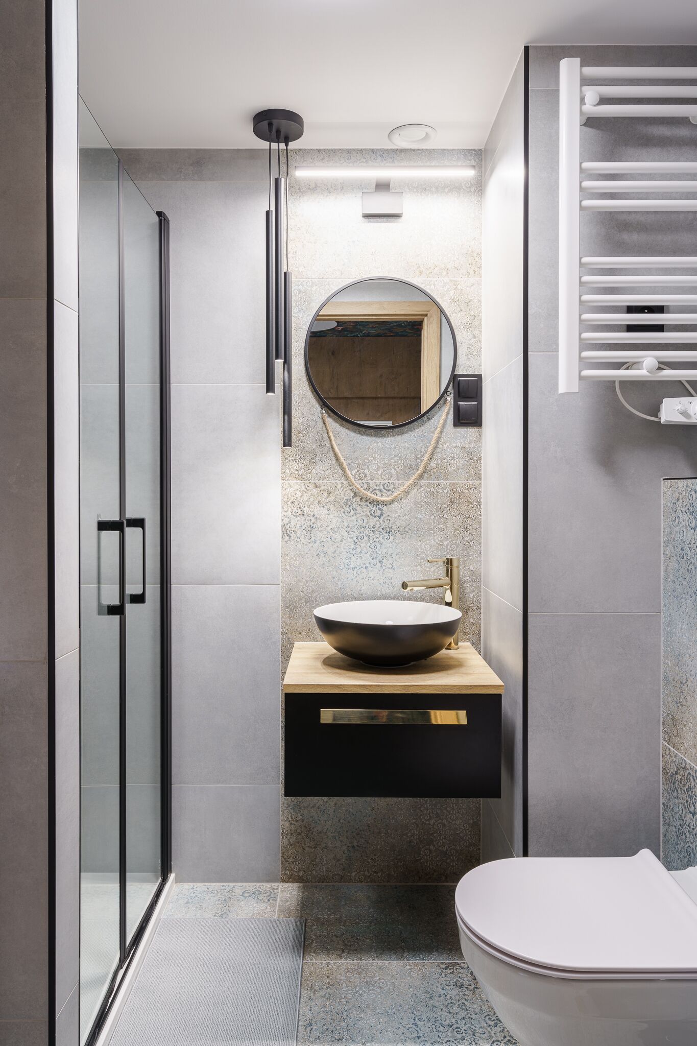 A modern bathroom with a glass shower enclosure, a freestanding sink with a round mirror, and a white toilet.