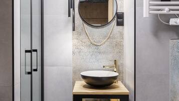 A modern bathroom with a glass shower enclosure, a freestanding sink with a round mirror, and a white toilet.