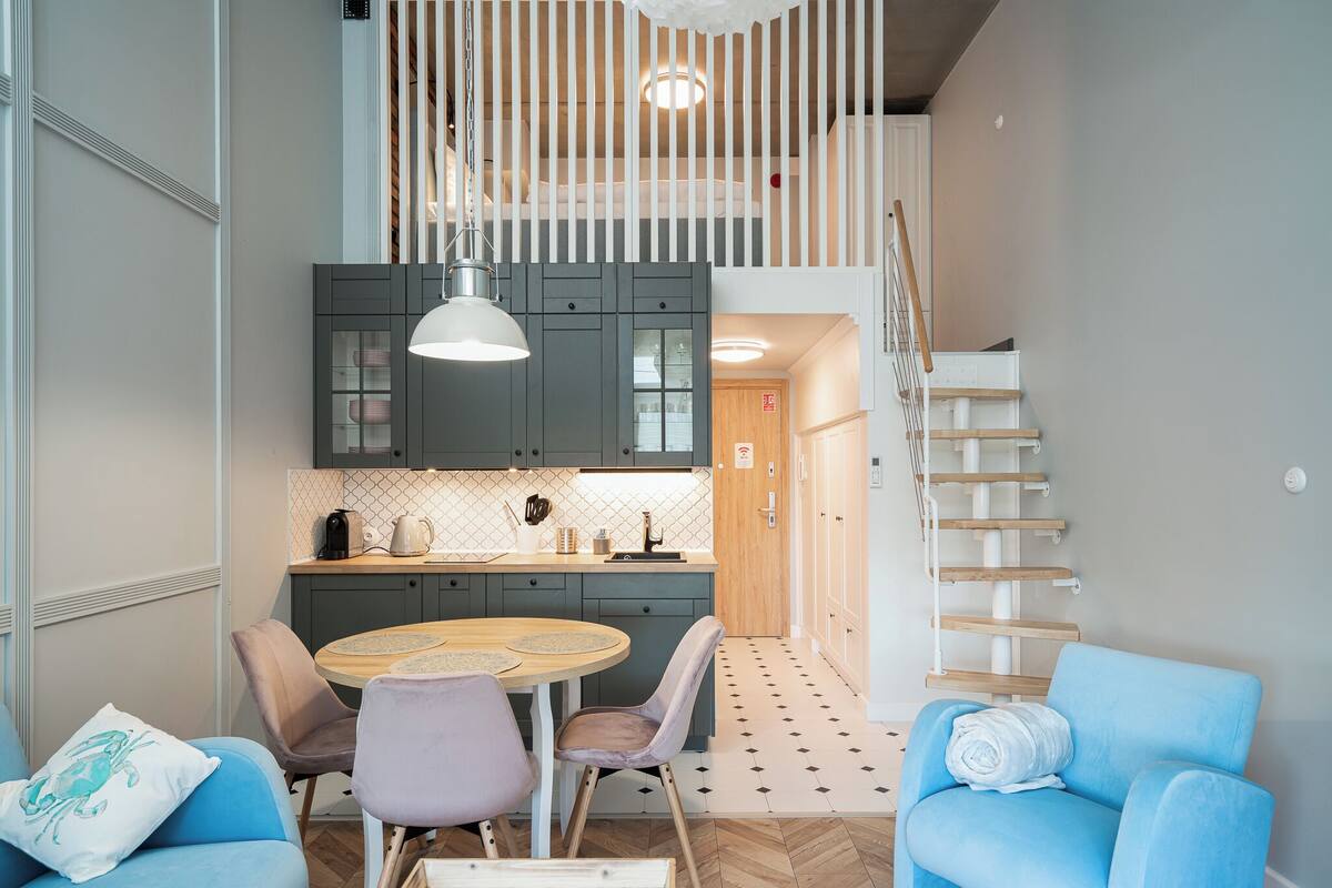 A modern kitchen with a dining area, wooden staircase, and a view of the living room.