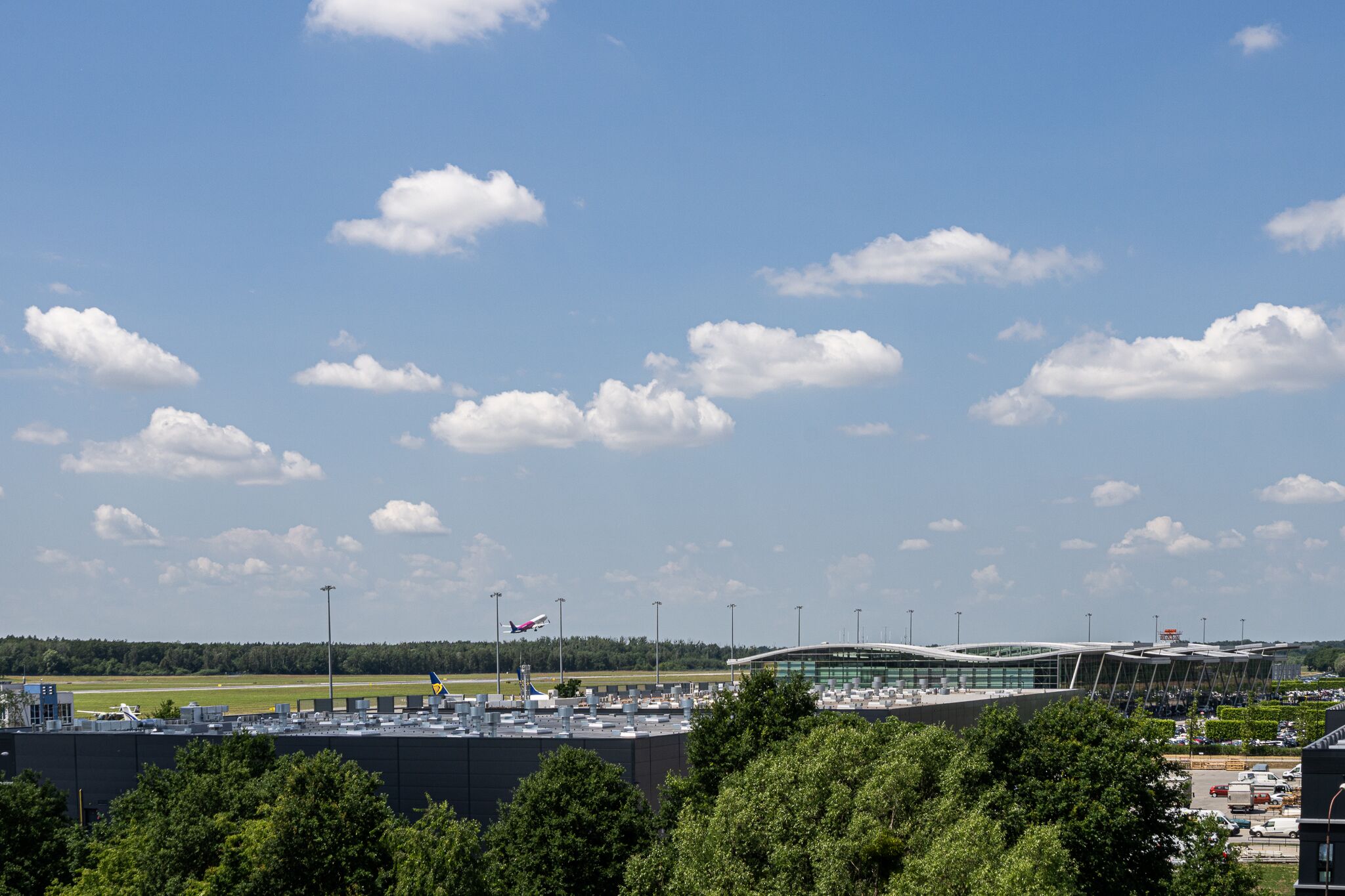 En flygplatsterminal med modern design, omgiven av grönska och en klar himmel.
