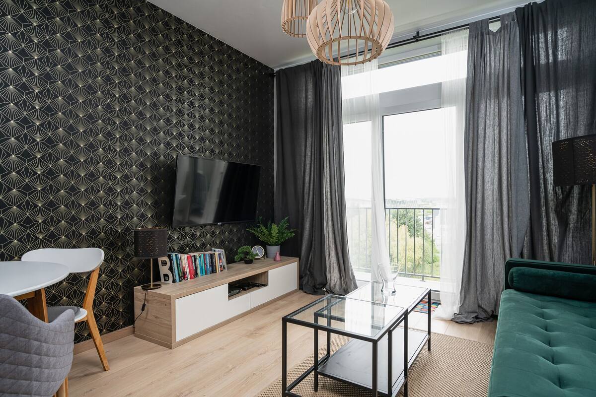 A modern living room with a flat-screen TV, a glass coffee table, a green sofa, and a white dining table with chairs.