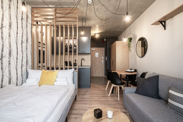 A modern hotel room with a bed, a sofa, a dining area, and a kitchen. - RentPlanet - Apartamenty Zarembowicza (Wroclaw)