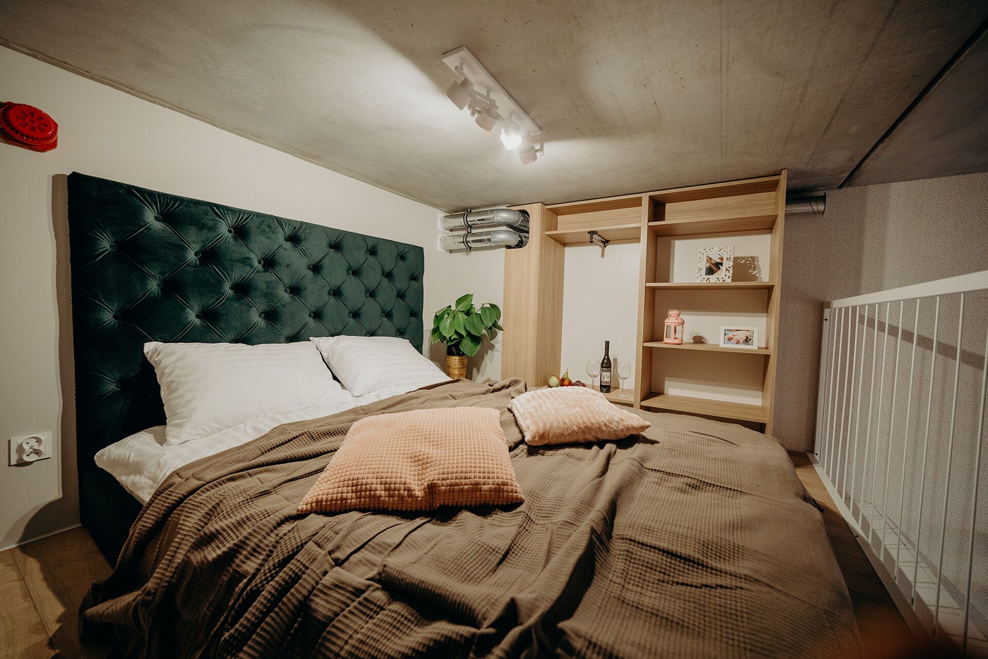 A bedroom with a tufted headboard, a bed with brown bedding, a bedside table with a plant, and a built-in shelving unit.