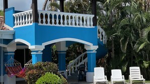 A pool area with a blue and white building, a hammock, and lounge chairs.