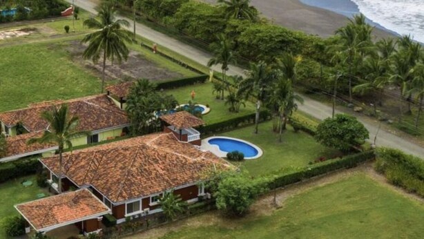 An aerial view of a coastal property with a swimming pool, beach access, and a road leading to the beach.