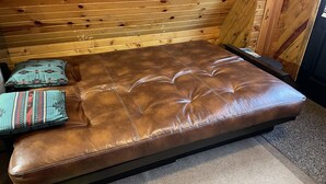 A brown leather sofa with tufted detailing, positioned against a wooden wall with horizontal slats.
