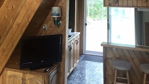A wooden interior with a TV, bar area, and a view through a glass door.