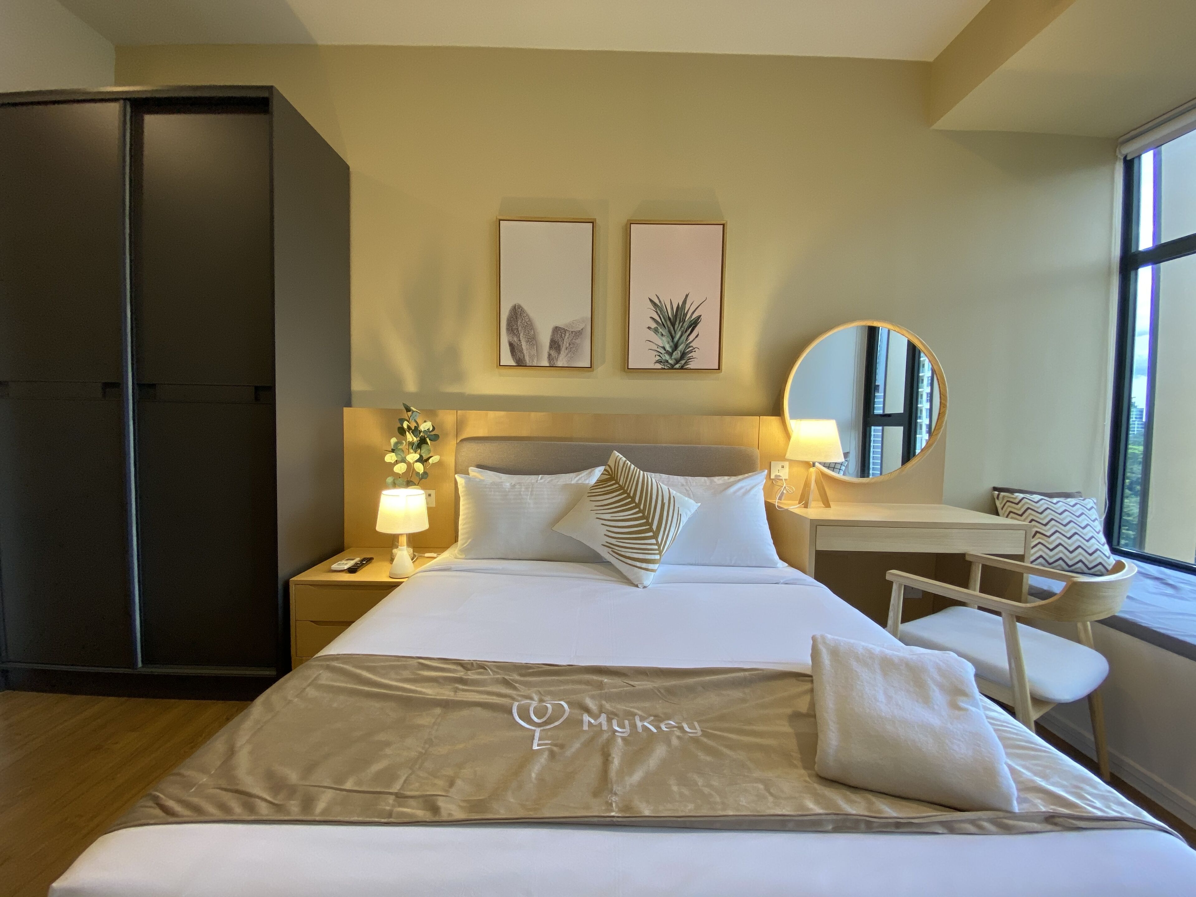 A hotel room with a bed, bedside tables, a desk, a chair, a wardrobe, and a large window.