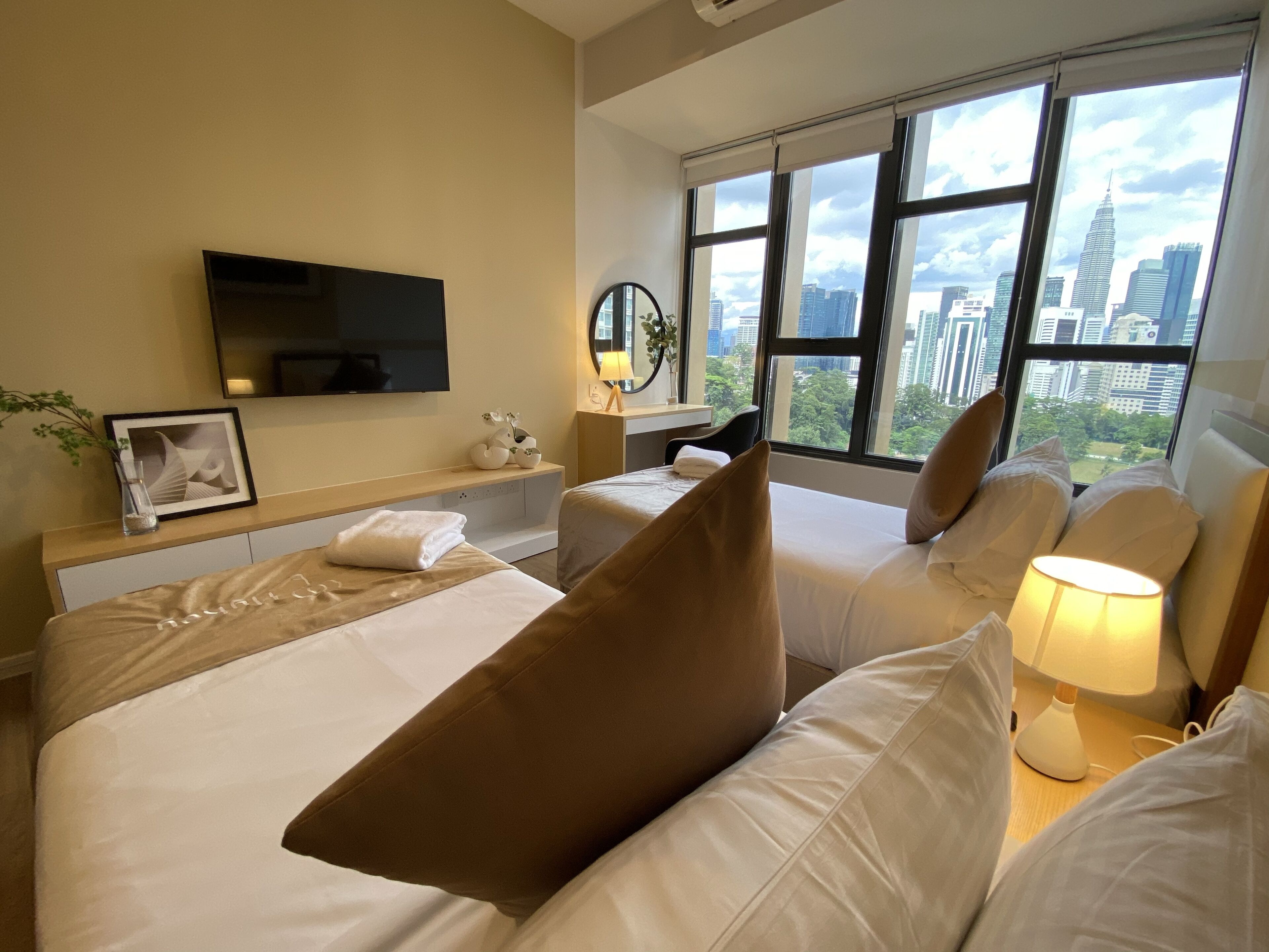 Quarto de hotel com cama, escrivaninha, televisão e uma grande janela com vista para a cidade.
